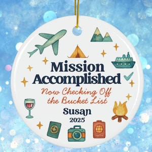 May include: White ceramic ornament with travel-themed illustrations, including an airplane, mountains, and a cruise ship. The text reads "Mission Accomplished, Now Checking Off the Bucket List, Susan 2025". Includes a gold string for hanging.