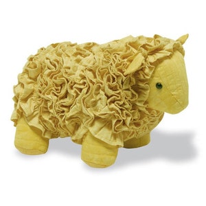 May include: A yellow plush sheep toy with a ruffled fabric body. The sheep has a small, pointed ear and a simple face with green eyes.