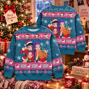 May include: A teal long-sleeve crewneck sweatshirt featuring a repeating pattern of cartoon characters, snowflakes, and reindeer. The text KPOP DEMON HUNTERS is printed on the chest. The design includes pink horizontal bands and Santa hat motifs.