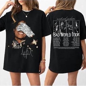 May include: Black t-shirt featuring a graphic of Michael Jackson with a sequined glove covering his face. The front of the shirt includes his signature and other design elements. The back of the shirt displays "Michael Jackson Bad World Tour" text and images.