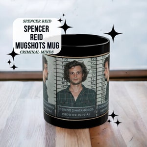 May include: Black mug featuring a white image of Spencer Reid from the TV show Criminal Minds. The image is a mugshot with the text "CERESO 2 MATAMOROS 13870-02-15-17-AJ" printed below.