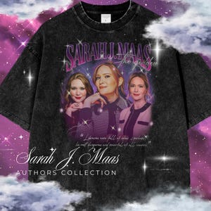 May include: Black acid wash t-shirt featuring a vintage-style graphic of three women with the text "SARAH J. MAAS the goddess" and "Authors Collection". The shirt has a crew neck and short sleeves. The graphic includes a quote.