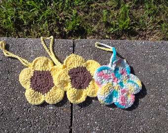May include: Three crocheted flower-shaped pot holders. Two are yellow with brown centers and one is multi-colored with pink, blue, and white.