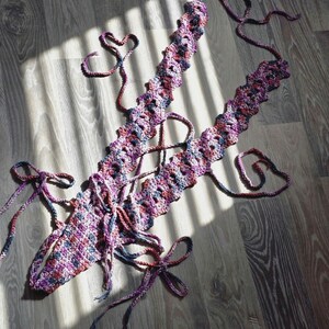 May include: A crocheted top with a pink, blue, and purple color scheme. The top has a lace-up design and is made with a chunky yarn.