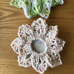 May include: Two crocheted flower-shaped coasters. One is white with pink and blue accents, the other is green and white.