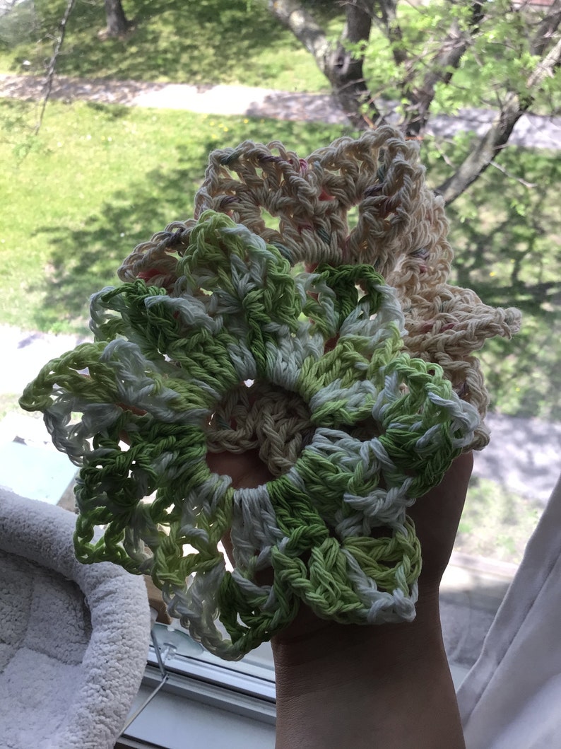 May include: Two crocheted doilies, one in green and white and the other in cream and pink, are stacked on top of each other.