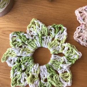 May include: A crocheted flower coaster in shades of green and white. The coaster is made with a delicate, lacy pattern and has a circular hole in the center.