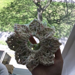 May include: A crocheted flower-shaped hair scrunchie in white with pink, green, and light blue accents.