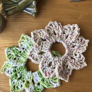 May include: Two crocheted flower-shaped coasters, one in green and white and the other in beige with pink and white accents.