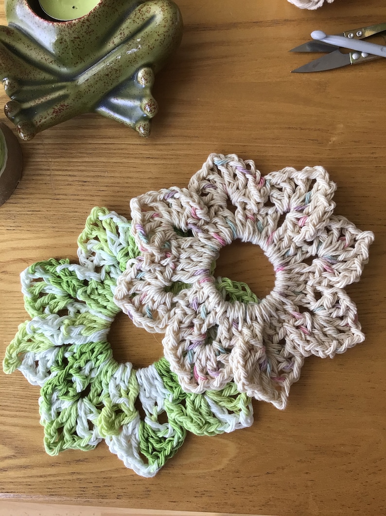May include: Two crocheted flower-shaped coasters, one in green and white and the other in beige with pink and white accents.