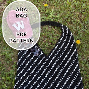 May include: Black and white striped crochet bag with a handle. The bag has a diagonal pattern and is lying on grass. Sunglasses rest on the bag. A pink baseball cap with a white "W" is visible. Text on the image reads "ADA BAG PDF PATTERN."