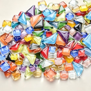 May include: A collection of small, smooth glass pieces in various shapes, including triangles and squares. The pieces feature a wide spectrum of translucent colours such as red, blue, green, yellow, orange, purple, and clear, with a polished finish.