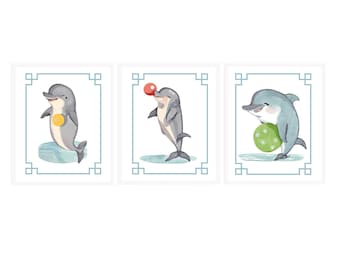Puede incluir: Tres ilustraciones de acuarela de delfines jugando con pelotas. El primer delfín sostiene una pelota amarilla, el segundo delfín equilibra una pelota roja en su nariz y el tercer delfín sostiene una pelota verde.