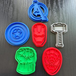 May include: Six different cookie cutters featuring popular superhero characters. The cutters are made of plastic and are blue, red, green, and gray. The characters include Captain America, Iron Man, Thor, Hulk, and Spiderman.