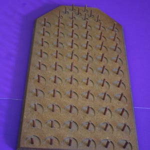 May include: A vintage wooden pegboard with a rectangular shape and rounded top. It features numerous small, brown pegs inserted into evenly spaced holes. The board is a light brown color.