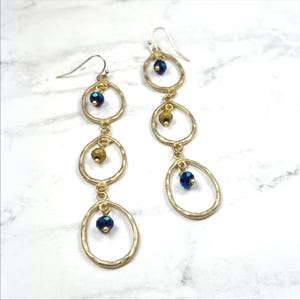 May include: Gold tone earrings with three oval hoops and blue and gold beads.