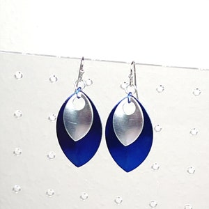 May include: A pair of silver and blue dangle earrings with a teardrop shape. The earrings have a silver top layer and a blue bottom layer.