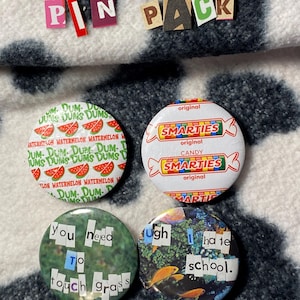 May include: A set of four circular pin-back buttons. One features a watermelon Dum Dums candy wrapper design, another a Smarties candy wrapper design, one with the text you need to touch grass, and one with the text ugh I hate school.