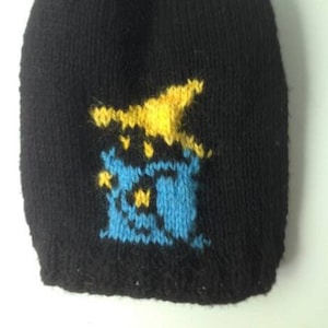 May include: Black knitted beanie with a yellow and blue pixelated design. The design features a yellow shape with a blue and yellow structure underneath.