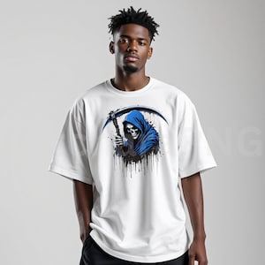 May include: White t-shirt featuring a graphic of the Grim Reaper in a blue hooded cloak, holding a scythe. The design includes black paint splatter effects. The shirt is a casual, oversized fit.