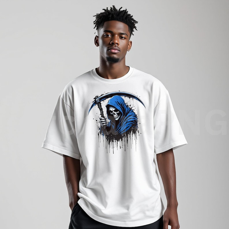 May include: White t-shirt featuring a graphic of the Grim Reaper in a blue hooded cloak, holding a scythe. The design includes black paint splatter effects. The shirt is a casual, oversized fit.
