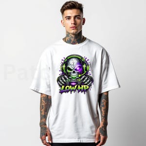 May include: White t-shirt featuring a skull graphic wearing headphones and holding a game controller. The skull has a purple eye and green accents. The text "LOW HP" is below the skull in green and purple.