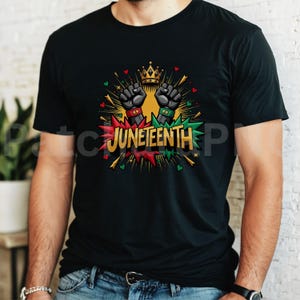 May include: Black t-shirt featuring a graphic design with the word "Juneteenth" in red, green, and gold. The design includes two raised fists, a gold crown, and colorful accents. The shirt is made of a soft material.