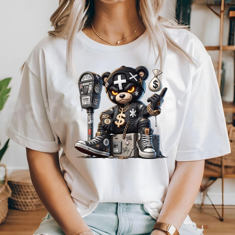 May include: White t-shirt featuring a cartoon bear character in a black leather outfit, gold chain, and sneakers. The bear is sitting on a concrete block next to a parking meter. The bear is pointing at a money bag.