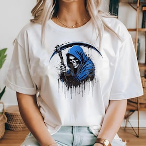 May include: White t-shirt featuring a graphic of a grim reaper with a blue hooded cloak and a scythe. The design includes black splatter effects. The reaper's skull is detailed with visible eye sockets and teeth.