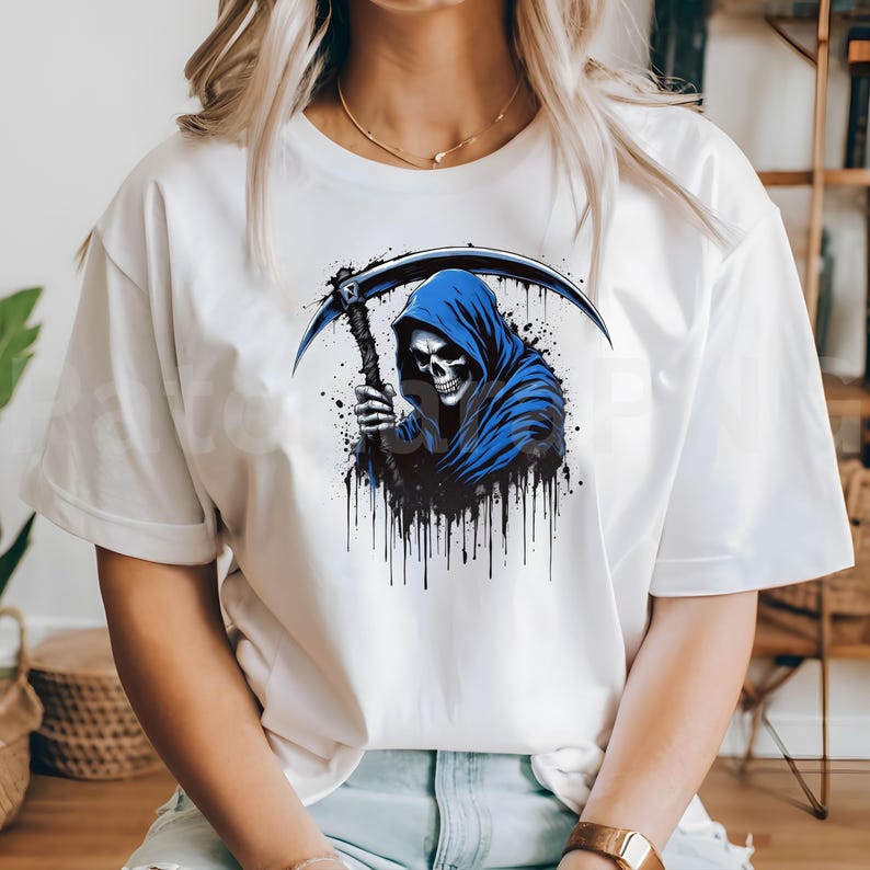 May include: White t-shirt featuring a graphic of a grim reaper with a blue hooded cloak and a scythe. The design includes black splatter effects. The reaper's skull is detailed with visible eye sockets and teeth.