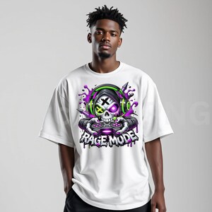 May include: White t-shirt featuring a skull graphic with headphones and a controller. The skull has purple and green accents, with the text "RAGE MODE" below. The design includes purple paint splatters.