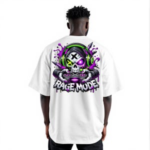 May include: White t-shirt featuring a skull graphic wearing headphones and holding a game controller. The design includes purple and green accents, with the words "Rage Mode" in a dripping font.