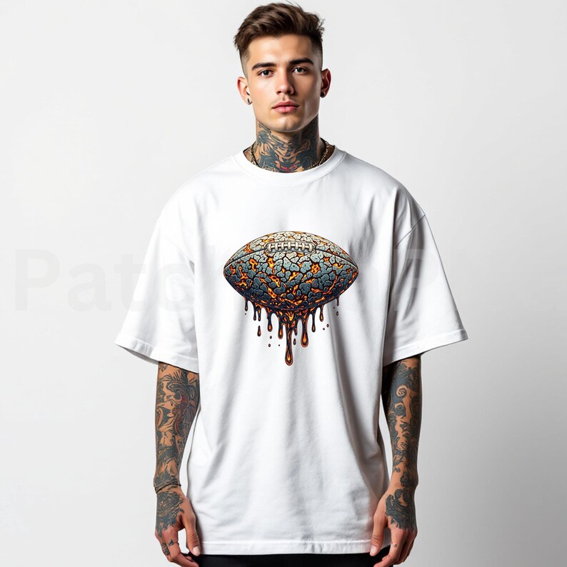 K&ouml;nnte beinhalten: Wei&szlig;es T-Shirt mit einem Football-Motiv. Das Football-Design hat ein rissiges, lavaartiges Aussehen mit Blau- und Oranget&ouml;nen und braunen Tropfdetails. Das T-Shirt hat kurze &Auml;rmel und eine lockere Passform.