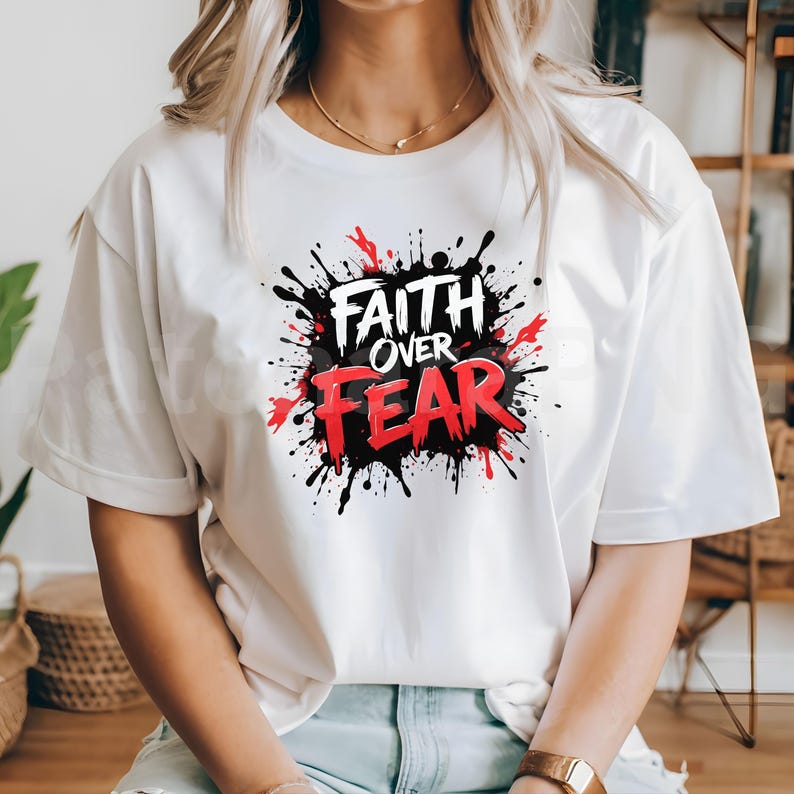 May include: White t-shirt featuring the text "FAITH OVER FEAR" in a bold, stylized design. The text is set against a black and red splatter effect, creating a dynamic and eye-catching graphic. The shirt is a casual wear item.