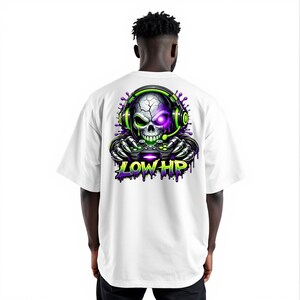 May include: White t-shirt featuring a vibrant graphic of a skull wearing a headset and holding a game controller. The skull has a purple eye and green accents, with the text "LOW HP" in green and purple. The design is centered on the back of the shirt.