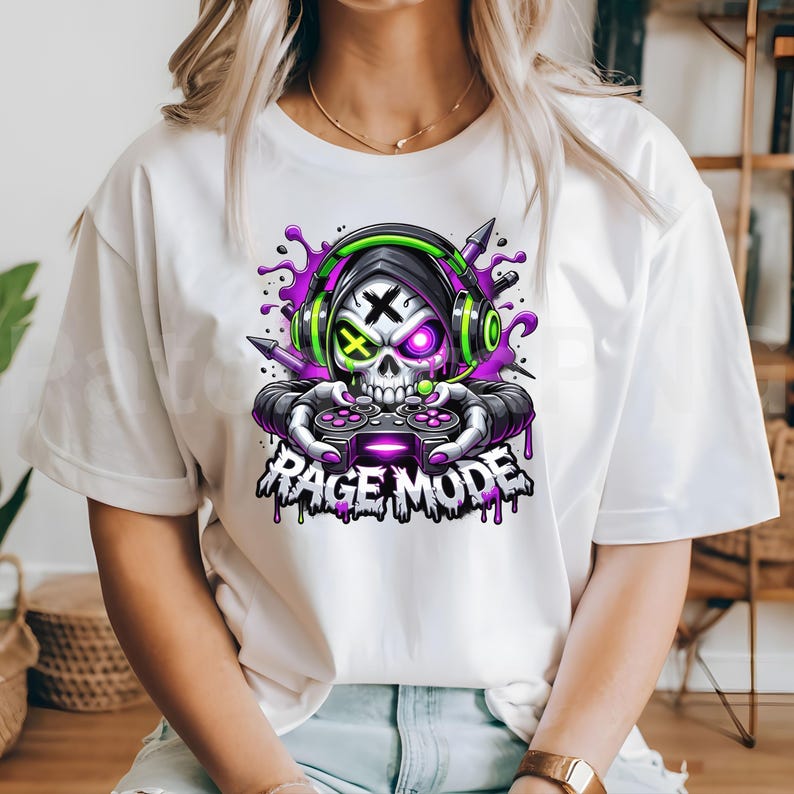May include: White t-shirt featuring a skull wearing headphones and holding a game controller. The skull has a purple and green design, with the text "RAGE MODE" below. The design includes purple paint splatters.