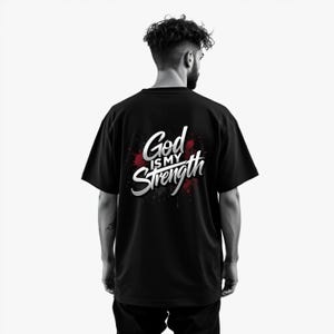 May include: Black t-shirt with the text "God is my Strength" in white and silver lettering, set against a red splatter design. The shirt is a crew neck style.