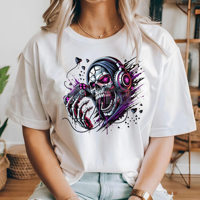 Peut inclure: T-shirt blanc avec une illustration num&eacute;rique d'un cr&acirc;ne portant un casque et tenant une manette de jeu. Le cr&acirc;ne a des yeux roses et est entour&eacute; d'&eacute;l&eacute;ments graphiques violets et noirs.