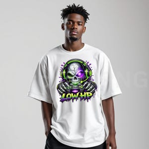 May include: White t-shirt featuring a skull graphic wearing headphones and holding a game controller. The skull has a purple eye and green accents. The text "LOW HP" is below the skull in green and purple.