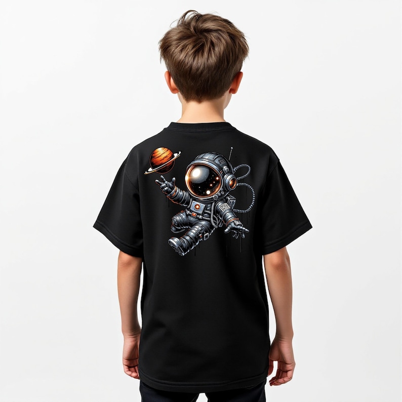 May include: Black t-shirt featuring a cartoon astronaut floating in space, with a planet in the background. The astronaut is wearing a detailed spacesuit with a reflective visor. The design is on the back of the shirt.