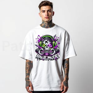 May include: White t-shirt featuring a skull graphic wearing headphones and holding a game controller. The skull has purple and green accents, with the words "RAGE MODE" below the skull in a dripping font.