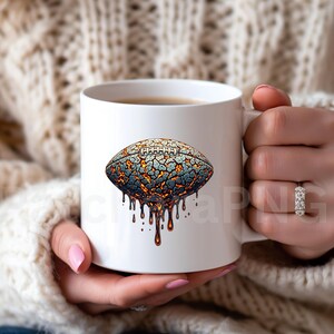K&ouml;nnte beinhalten: Wei&szlig;e Keramiktasse mit einem stilisierten American-Football-Design. Das Design zeigt eine rissige, strukturierte Oberfl&auml;che in Grau, Blau und Orange mit tropfenden, geschmolzenen Elementen. Die Tasse wird von einer Person gehalten.
