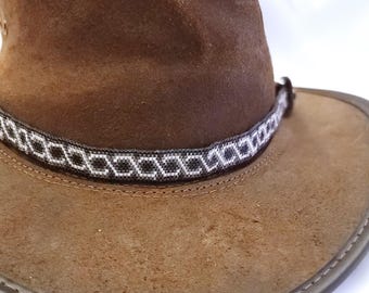 Op de afbeelding: Een bruine leren cowboyhoed met een wit en zwart gepatroneerd bandje rond de kroon.