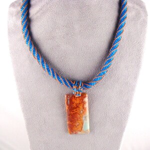 May include: A blue and copper beaded necklace with a rectangular pendant made of brown and white agate.