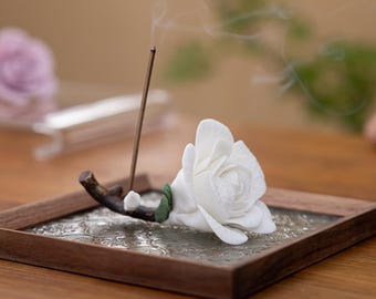 May include: A handmade ceramic flower incense holder. The white rose is set on a square wooden tray with a decorative glass insert. The incense stick is lit, with smoke rising. The text on the image reads "Incense holder handmade ceramic flower."