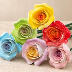 Puede incluir: Una colección de seis rosas artificiales con pétalos lisos y brillantes en tonos vibrantes de amarillo, verde lima, azul claro, rojo, lavanda y rosa suave. Cada flor presenta un centro en espiral y está unida a un tallo verde delgado.