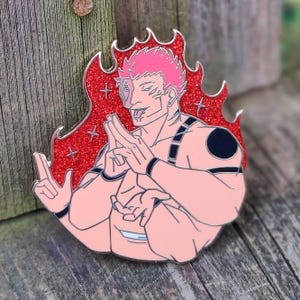 Könnte beinhalten: Emaille-Anstecknadel mit einem muskulösen Charakter mit rosa Haaren und Haut, vor einem roten Glitzerflammendesign. Die Figur macht Handgesten, mit schwarzen Akzenten auf Schultern und Armen. Die Anstecknadel hat eine silberne Umrandung.