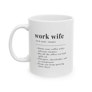 Op de afbeelding: Witte keramische mok met de tekst "work wife" in het zwart en een definitie. De definitie bevat de zinnen "Kent je koffiebestelling", "Heeft alle thee van het kantoor" en "Houdt je van stoppen".
