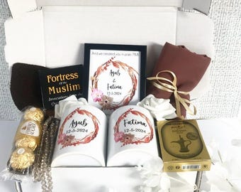 May include: A white gift box filled with a variety of items, including two white mugs with the names "Ayub" and "Fatima" and the date "12-5-2024" printed on them, a brown scarf, a book titled "Fortress of the Muslim", a string of prayer beads, a box of chocolates, and a small box of incense. The box also includes a framed print with the names "Ayub & Fatima" and the date "12-5-2024" printed on it.