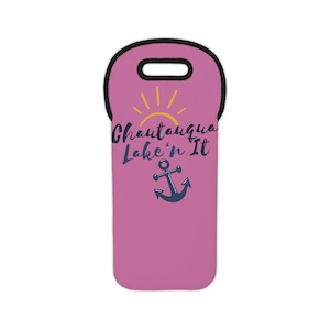 Pode incluir: Bolsa de neoprene rosa para garrafa de vinho com alça preta. A bolsa tem um design gráfico de um sol amarelo, uma âncora e o texto "Chautauqua Lake'n It".